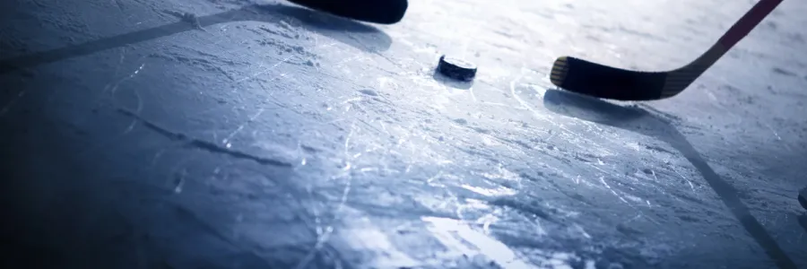 two hockey sticks and puck facing off on ice